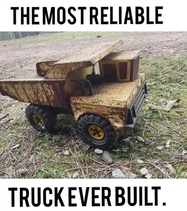 A heavily rusted, weathered yellow toy dump truck, branded 'Mighty Toys', sits abandoned on a patch of grass and dirt. The…