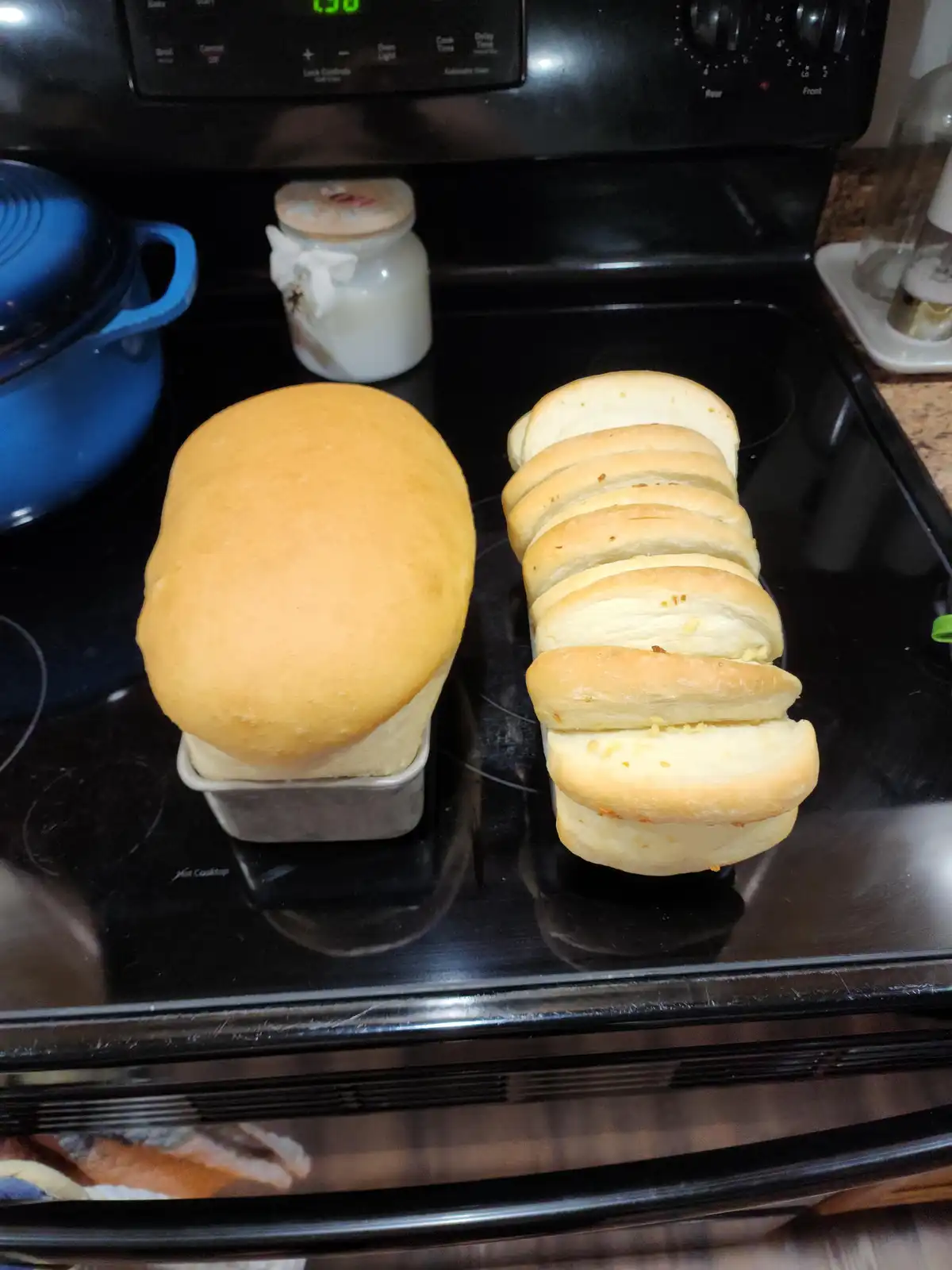 Two loaves of bread sit on a black stovetop; one is whole and rounded, the other is sliced into individual rolls. The text…