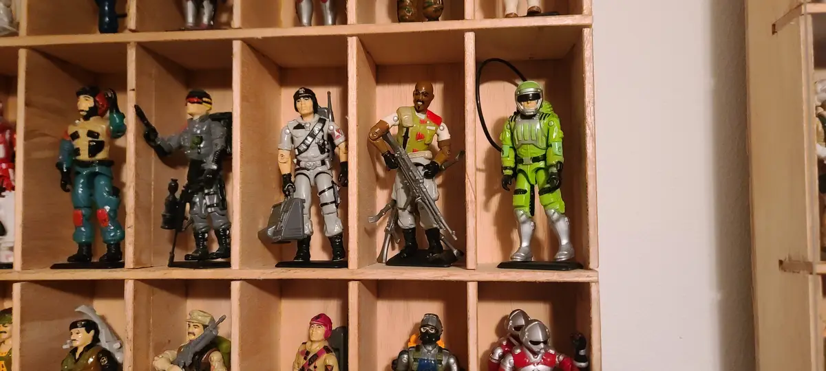A wooden display shelf holds multiple rows of action figures in individual compartments. The top row features five distinct…
