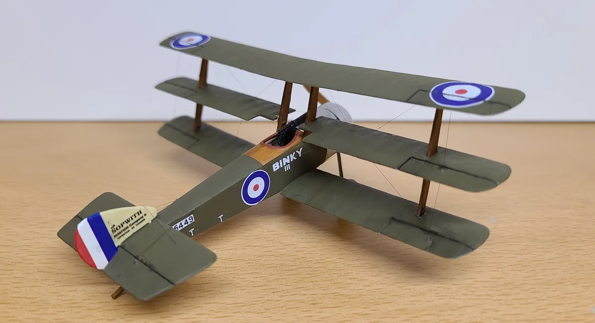 A detailed model of a green British Sopwith biplane with roundel insignia on its wings and fuselage, resting on a wooden…