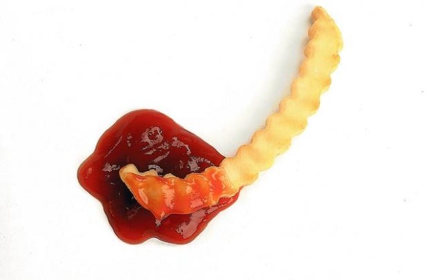 A single crinkle-cut french fry is dipped into a dollop of ketchup on a plain white background. The text 'ketchup' is…