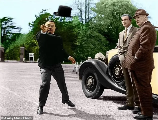 a man in a black suit and top hat is mid-motion, tossing his top hat into the air while standing on a paved road. Behind…