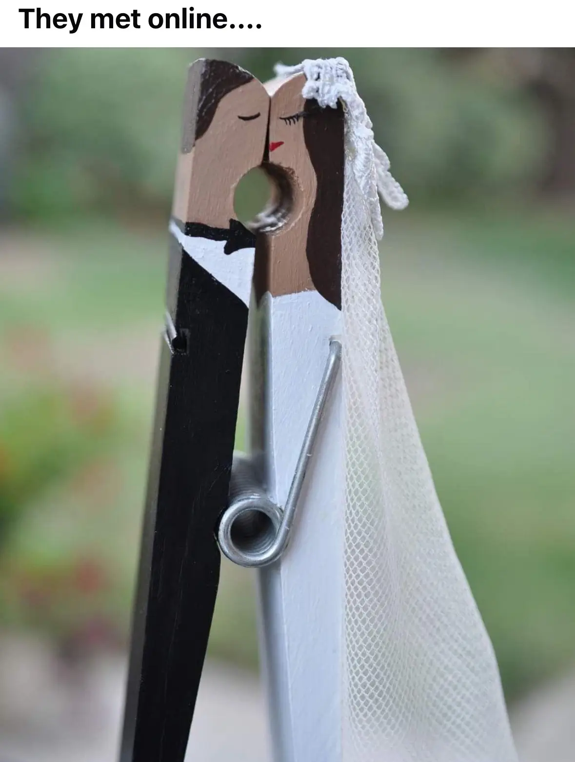 A close-up of a wooden clothespin painted to resemble a bride and groom kissing. The groom side is painted in black tuxedo…