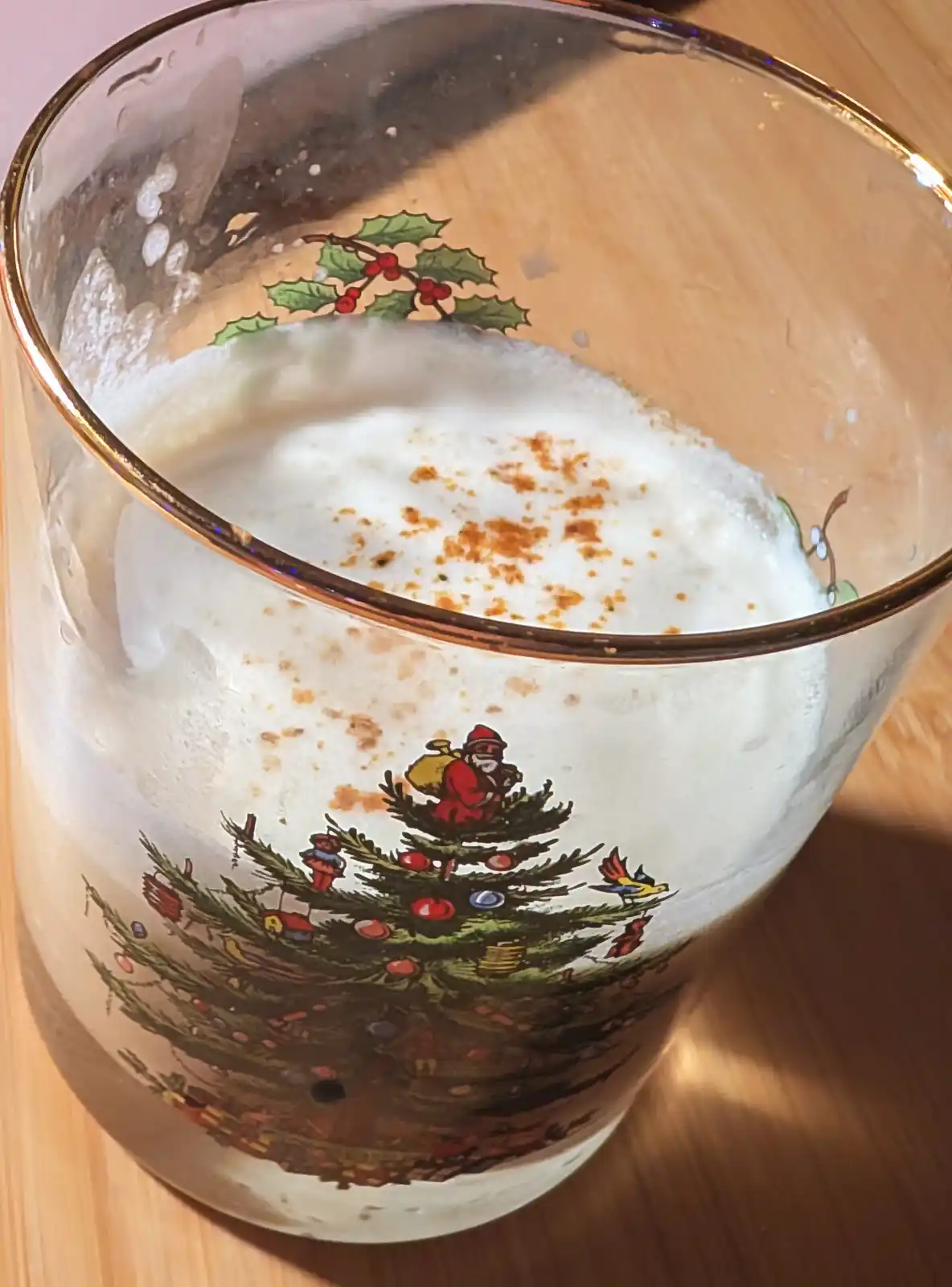 A close-up of a frothy, creamy beverage in a glass decorated with a Christmas tree and Santa Claus, with a holly design near…