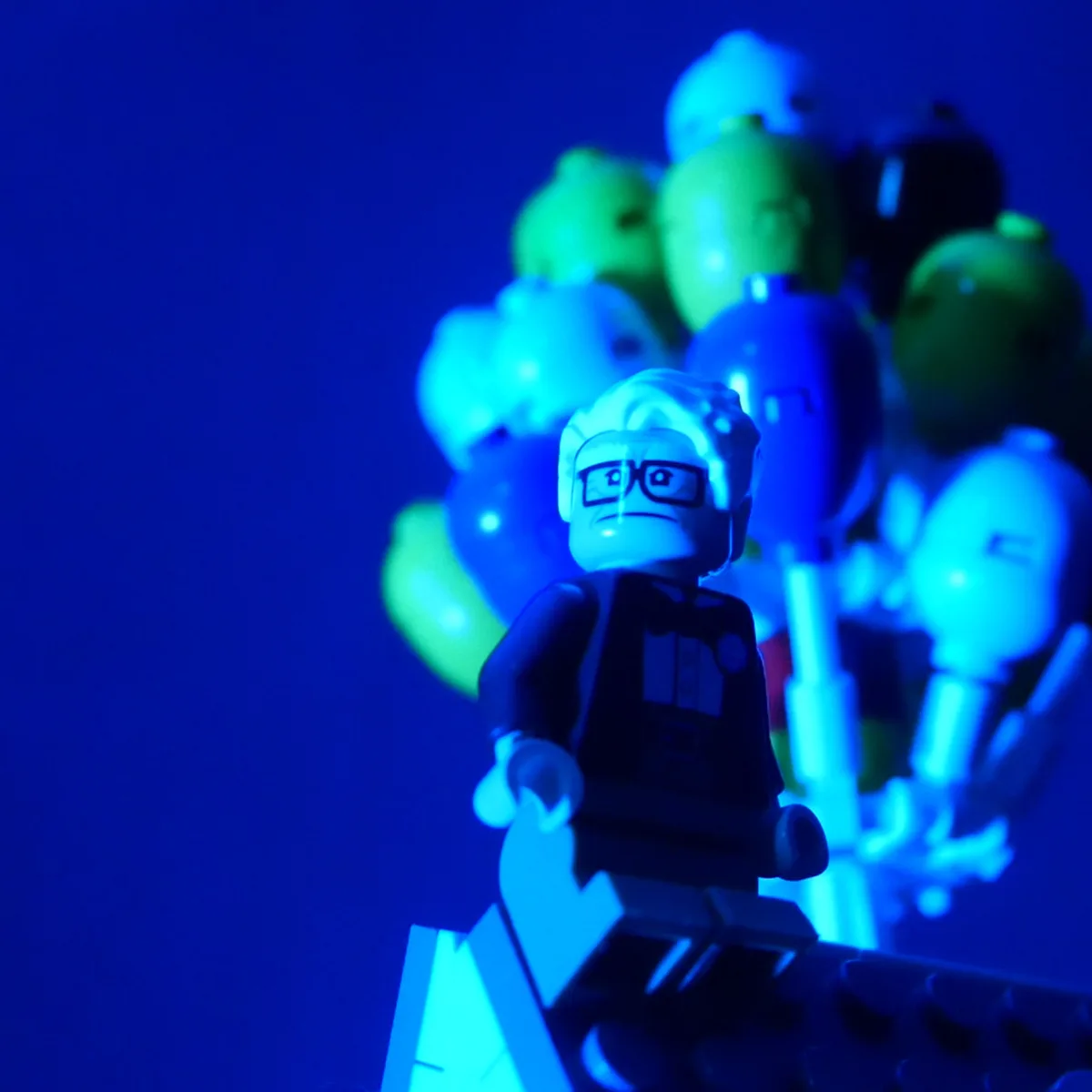 A close-up of a LEGO minifigure with glasses and a stern expression, illuminated by blue light, stands in front of a blurred…