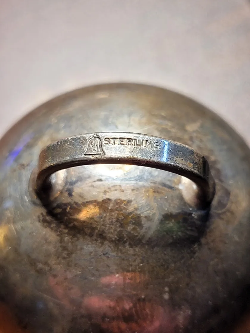 A close-up photo shows a tarnished, silver-colored metal ring embedded in the center of a round, dull metal object, possibly…