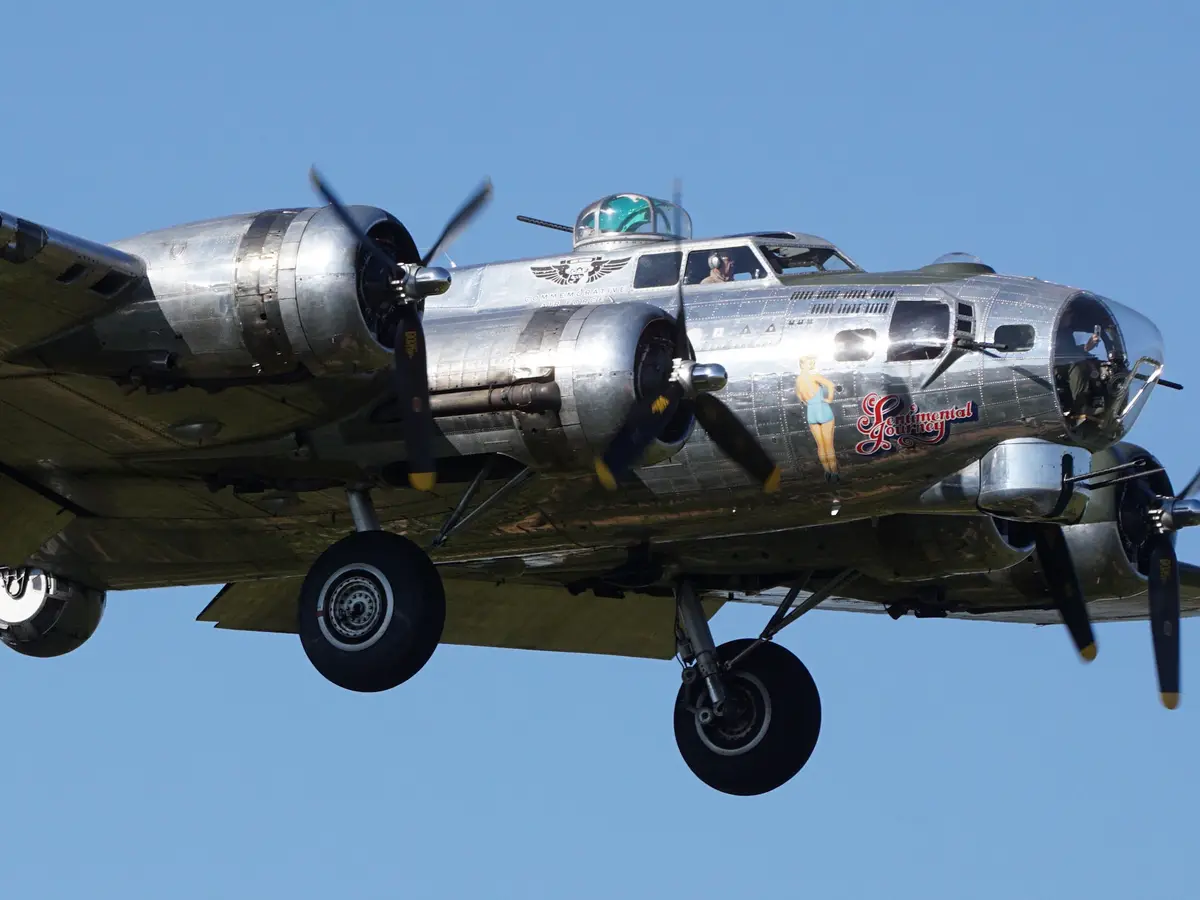 A silver WWII-era B-17 Flying Fortress bomber, named 'Sentimental Journey', is captured in flight against a clear blue sky…