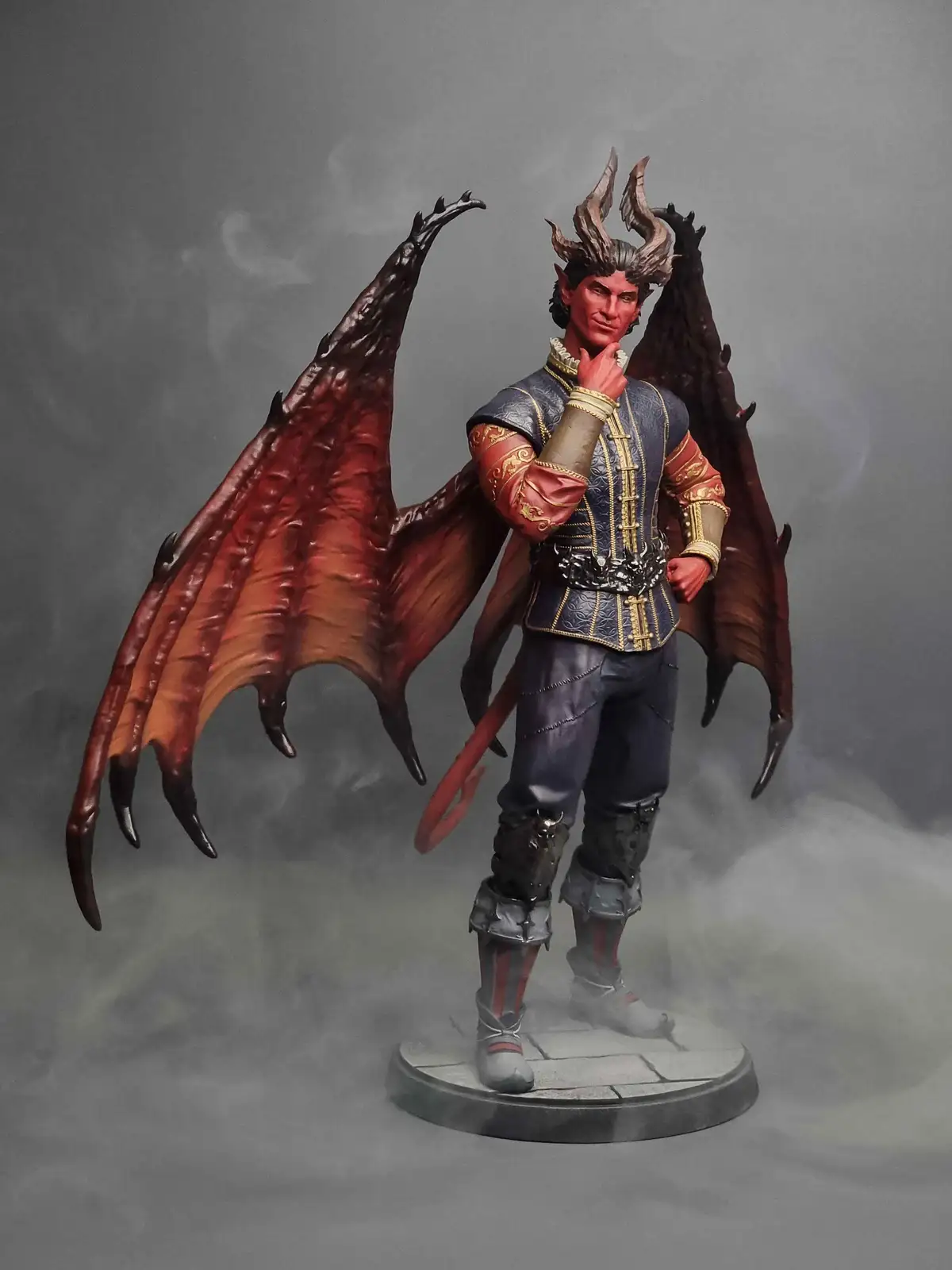 A detailed figurine of a demonic character with large red bat-like wings, horns, and a tail, dressed in ornate blue and gold…
