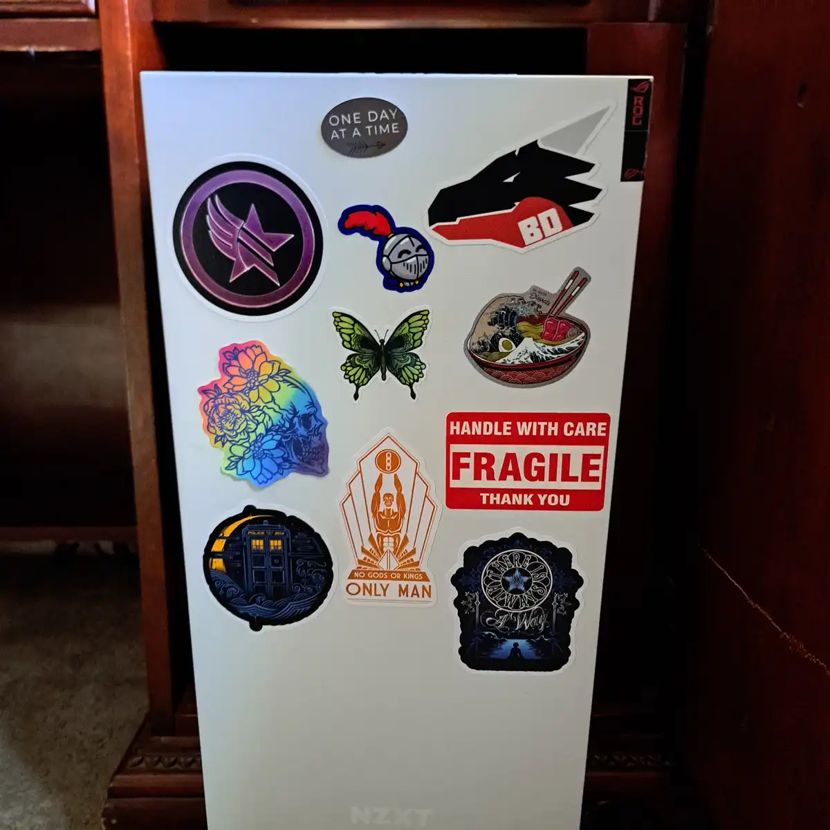 A white rectangular box, likely a computer case, is covered in various colorful stickers including a dragon, a butterfly, a…