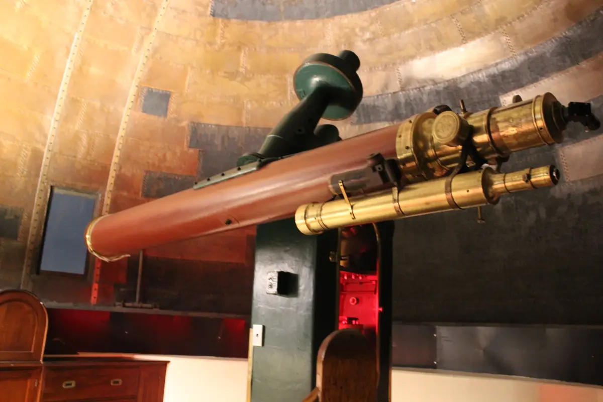 A large, vintage-style telescope with a long reddish-brown tube and brass fittings is mounted horizontally inside a domed…