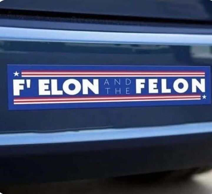 A close-up of a blue bumper sticker on a dark car, featuring red and white stripes and stars, with the text 'F' ELON AND THE…