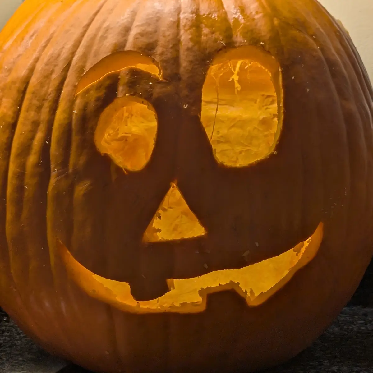 A close-up of a carved Halloween pumpkin with one perfectly round eye and one irregular, jagged oval eye, illuminated from…