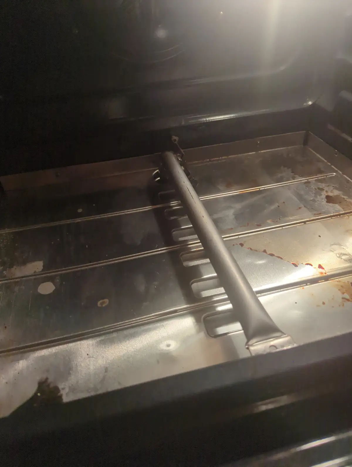 A close-up photo of the inside of a stainless steel oven, showing a metal rack and dirty bottom with brown stains and food…