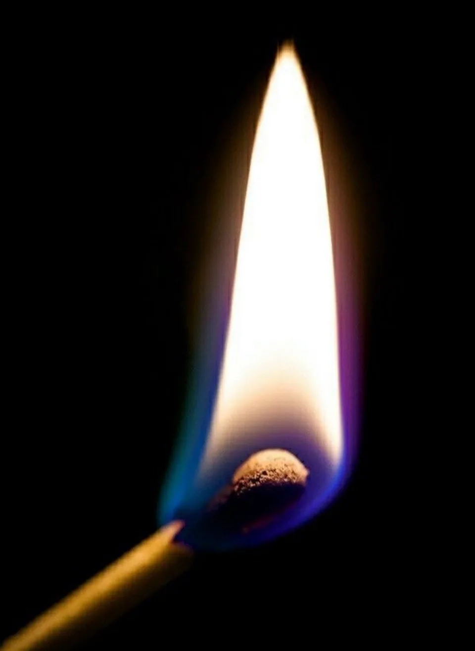 A close-up photograph of a single lit matchstick against a black background, showing its bright yellow-white flame with a…