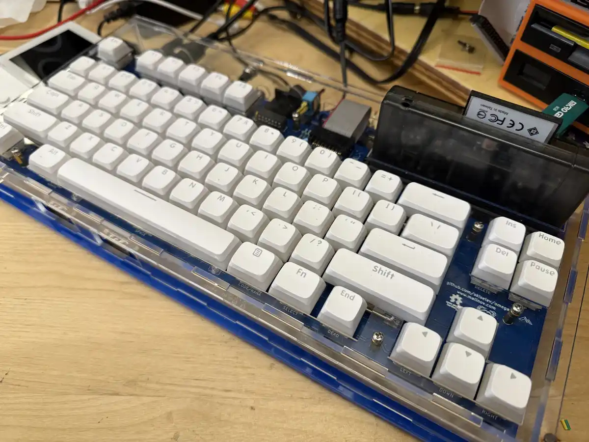 A close-up photo of a white mechanical keyboard with a transparent case, revealing its blue circuit board and internal…