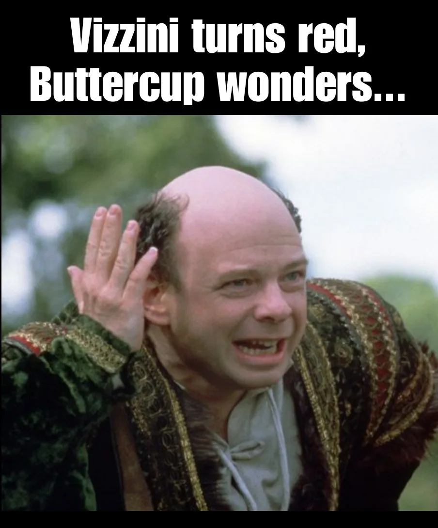 A still image of the character Vizzini from The Princess Bride, shown with a bald head and sparse hair, wearing a green and…
