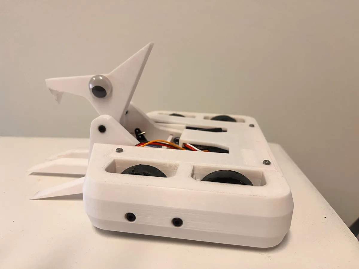 A white 3D-printed robot with a shuriken (throwing star) shape, featuring a googly eye on its pointed tip and exposed…