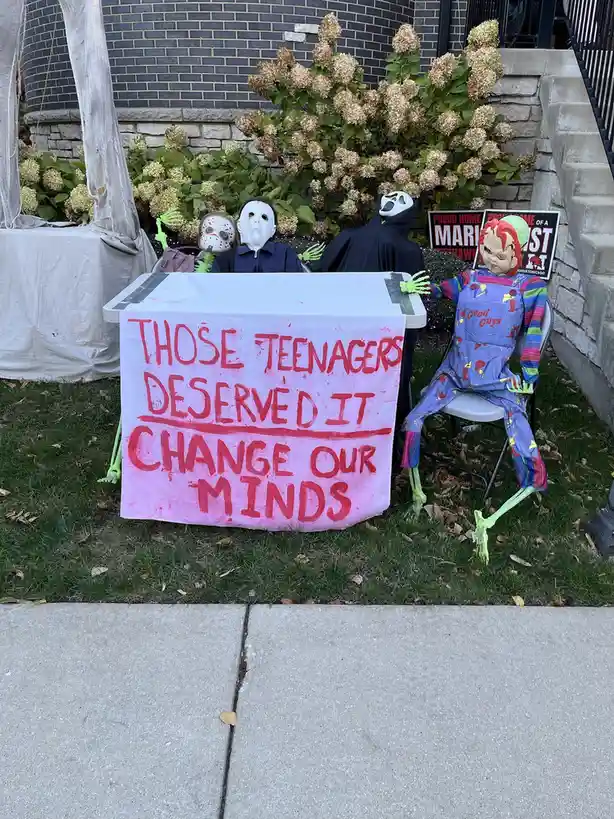 A Halloween yard display features four horror movie character figures—Jason, Michael Myers, Ghostface, and Chucky—seated…