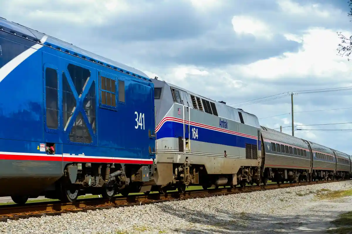 A blue and silver Amtrak train with locomotives numbered 341 and 164 is shown on tracks under a cloudy sky. The overlaid…