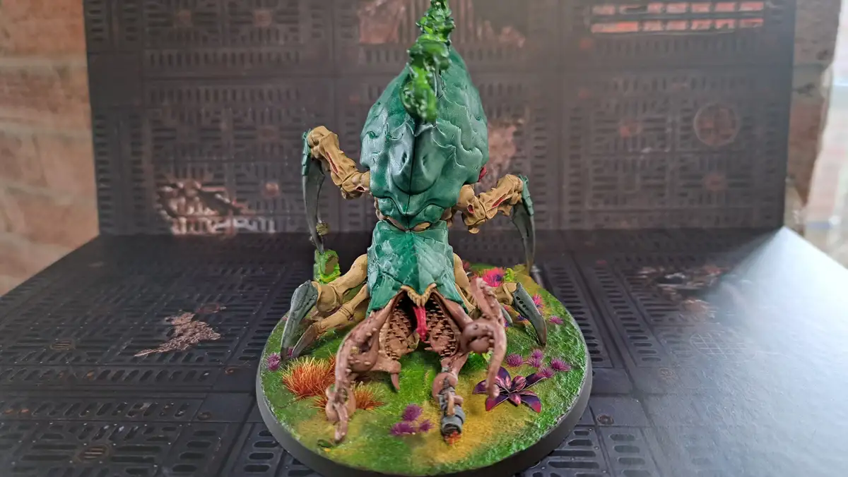 A painted miniature of a grotesque, plant-like creature with a green, leafy, skull-like head and multiple clawed limbs…