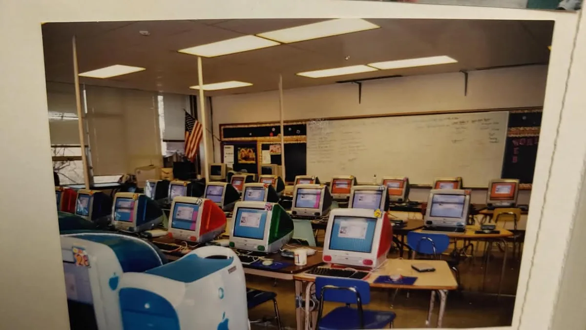A vintage photo shows a classroom filled with rows of old Apple iMac G3 computers from the late 1990s, identifiable by their…