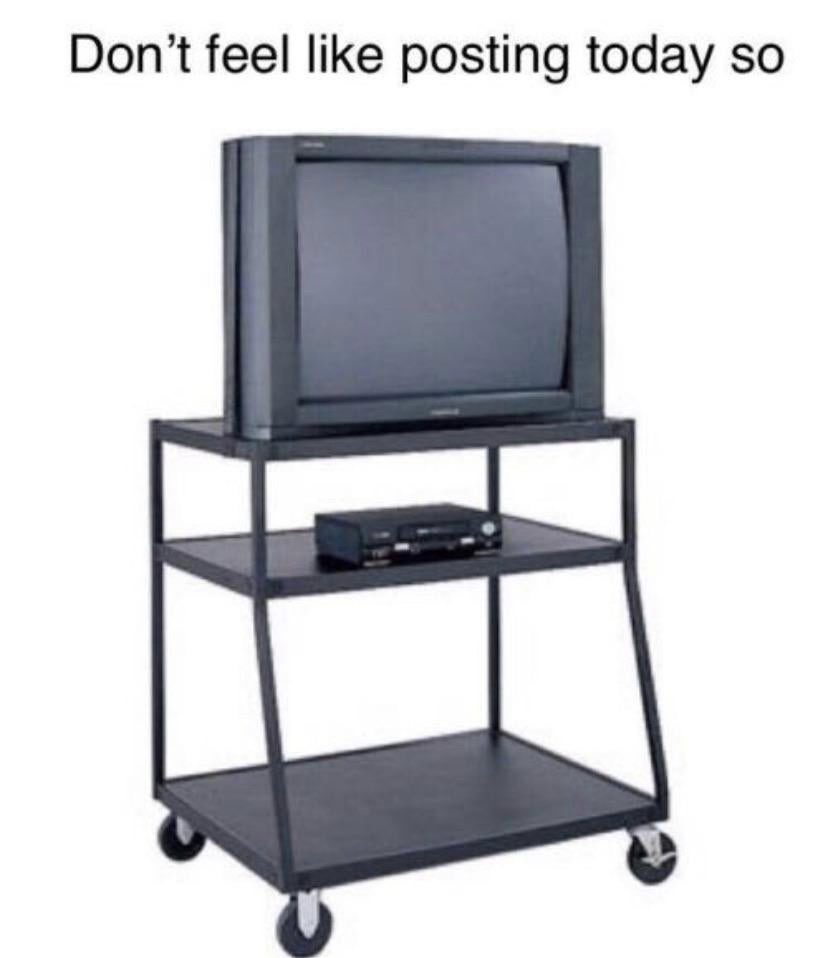A black, three-tiered rolling TV cart with wheels holds an old CRT television on the top shelf and a VCR on the middle…