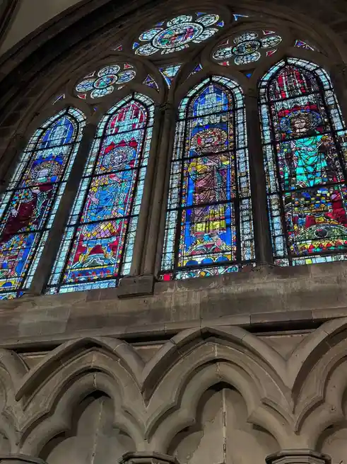 A photo of ornate, colorful stained glass windows inside a Gothic-style church, featuring religious figures and intricate…