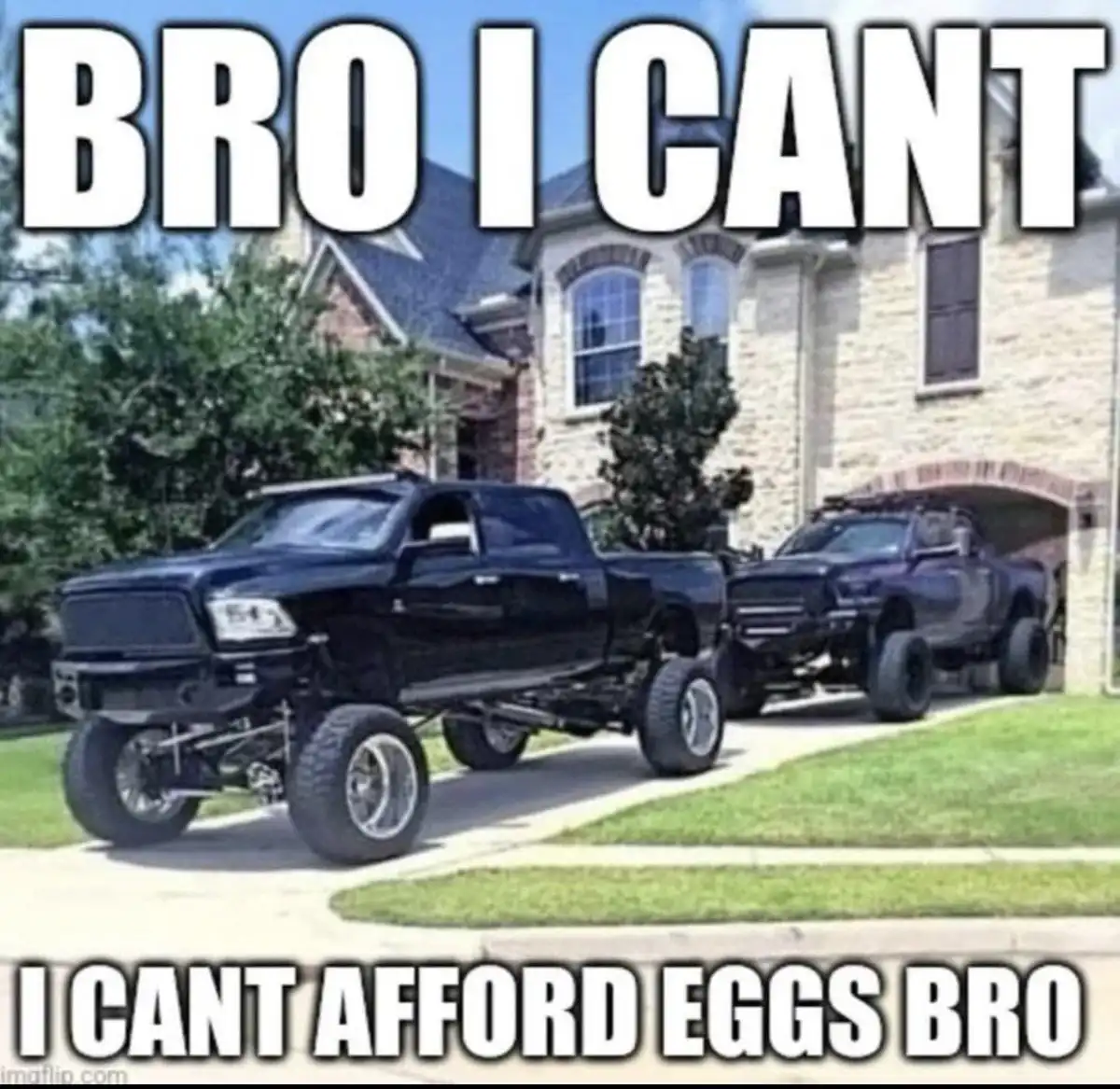 Two large, heavily modified black pickup trucks are parked in front of a large, expensive-looking stone house with a garage…