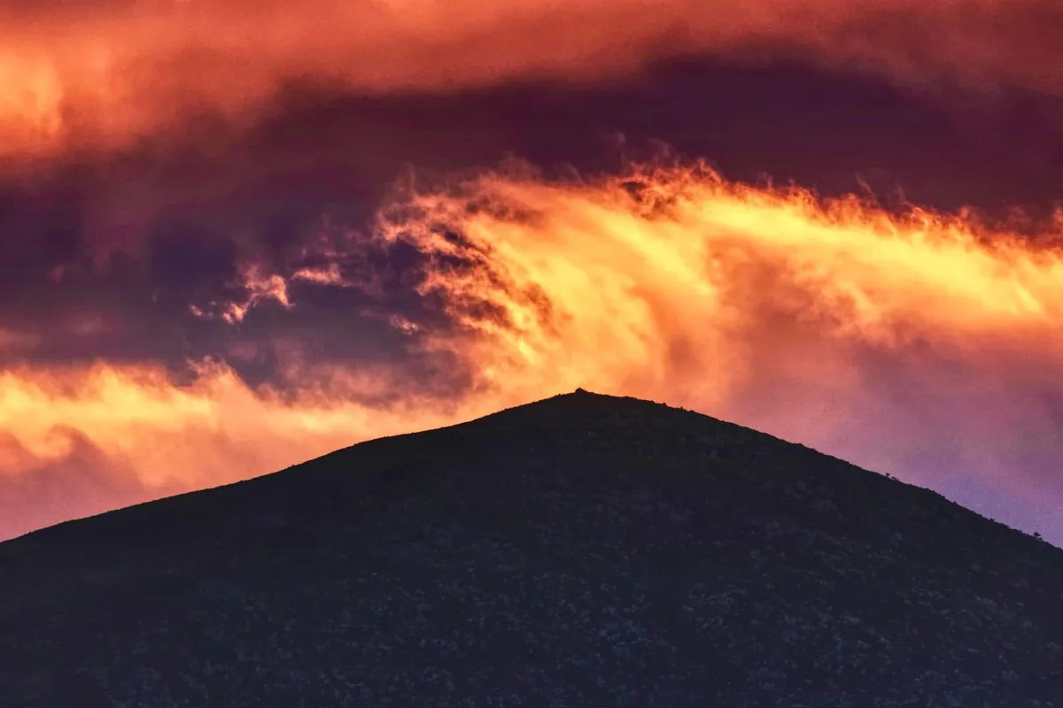 A dramatic sky with fiery orange and purple clouds above the silhouette of a dark mountain peak. The overlaid text reads…