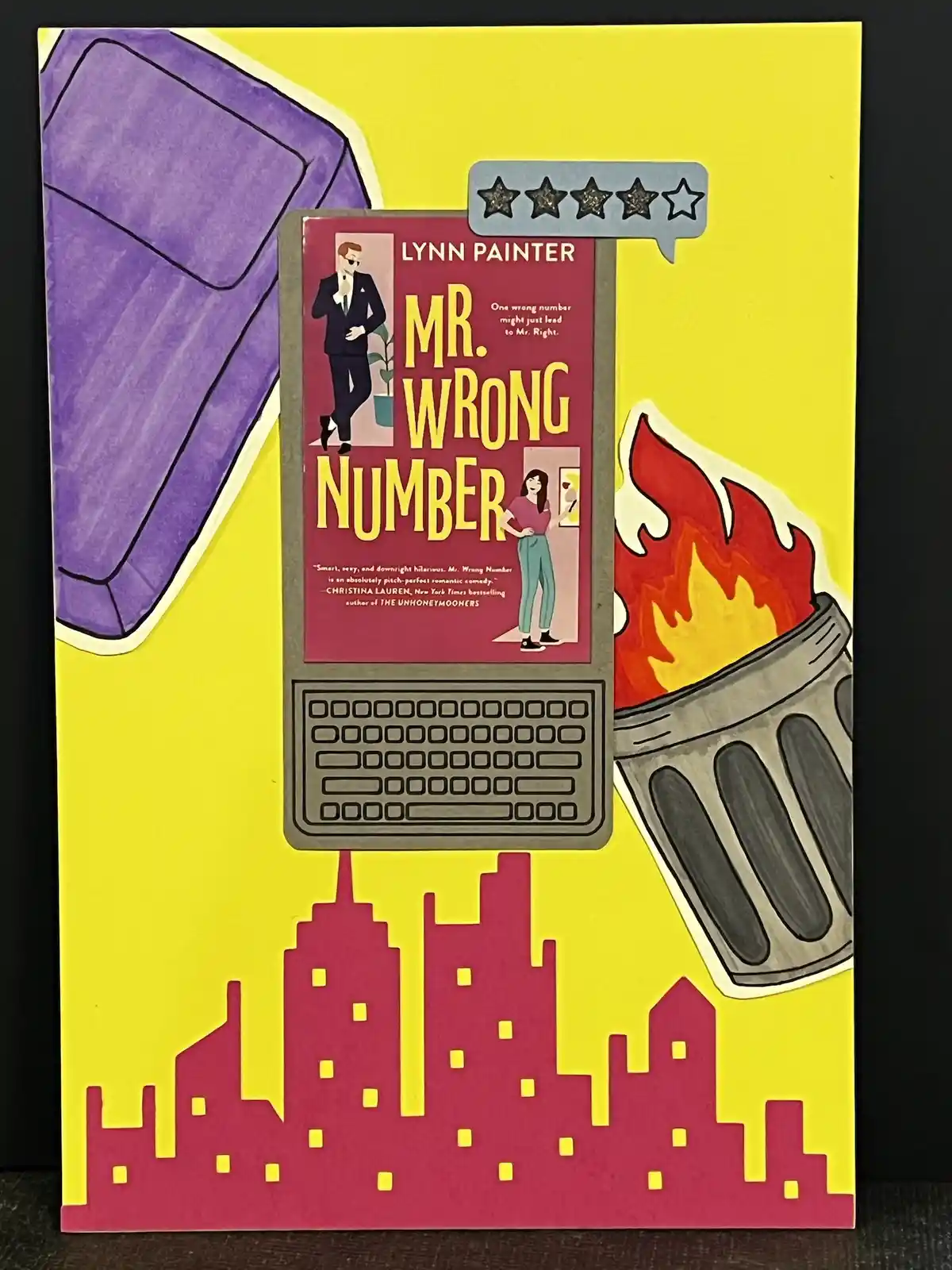 A cartoon-style image shows a book titled 'Mr. Wrong Number' by Lynn Painter displayed on a laptop screen, with a speech…