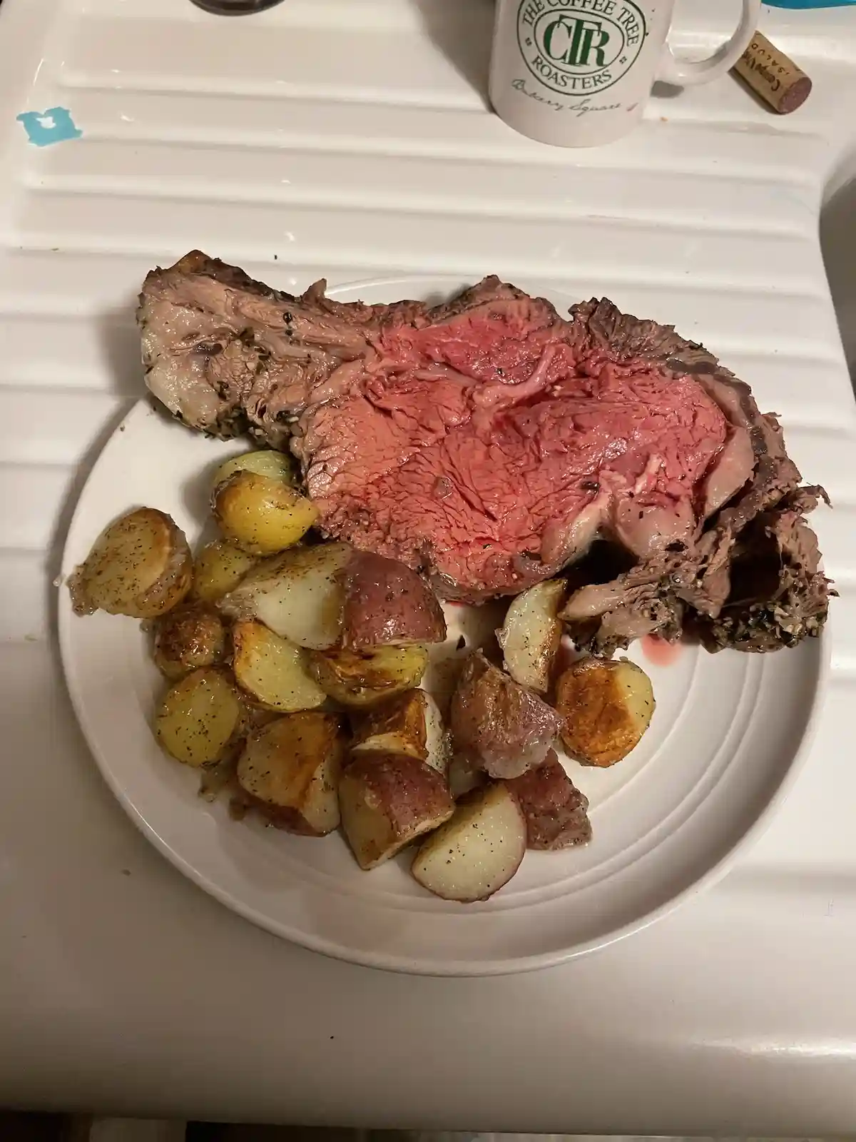 A plate of sliced roast beef with a visible pink center, accompanied by roasted potatoes, sits on a white countertop. In the…