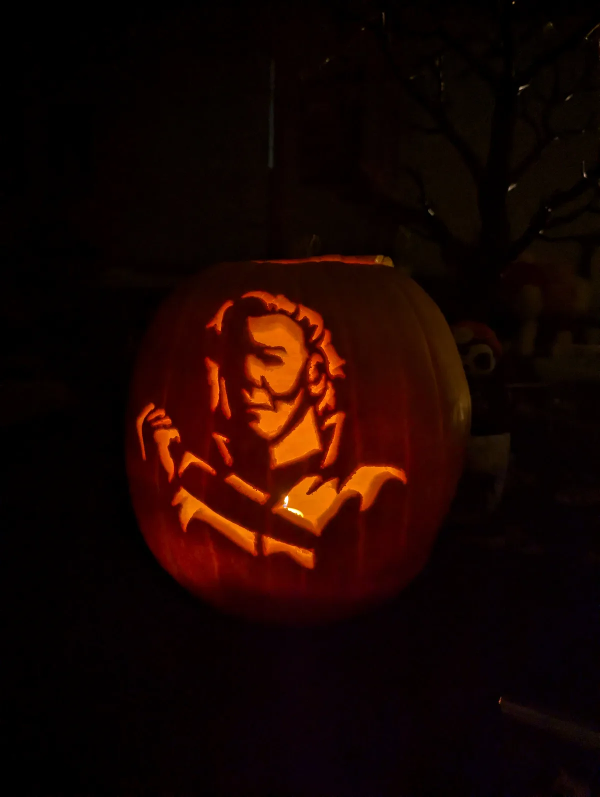 A carved Halloween pumpkin illuminated from within, featuring a detailed portrait of a man with long hair and a beard…