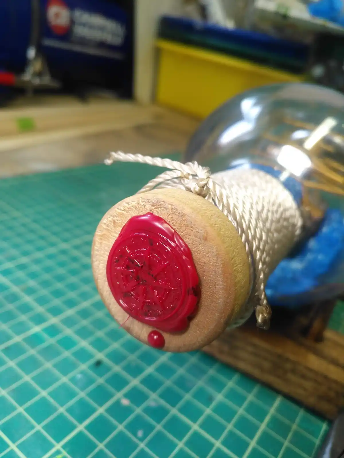A close-up of a glass bottle sealed with a red wax seal featuring an intricate star-like design, tied with a thick rope…