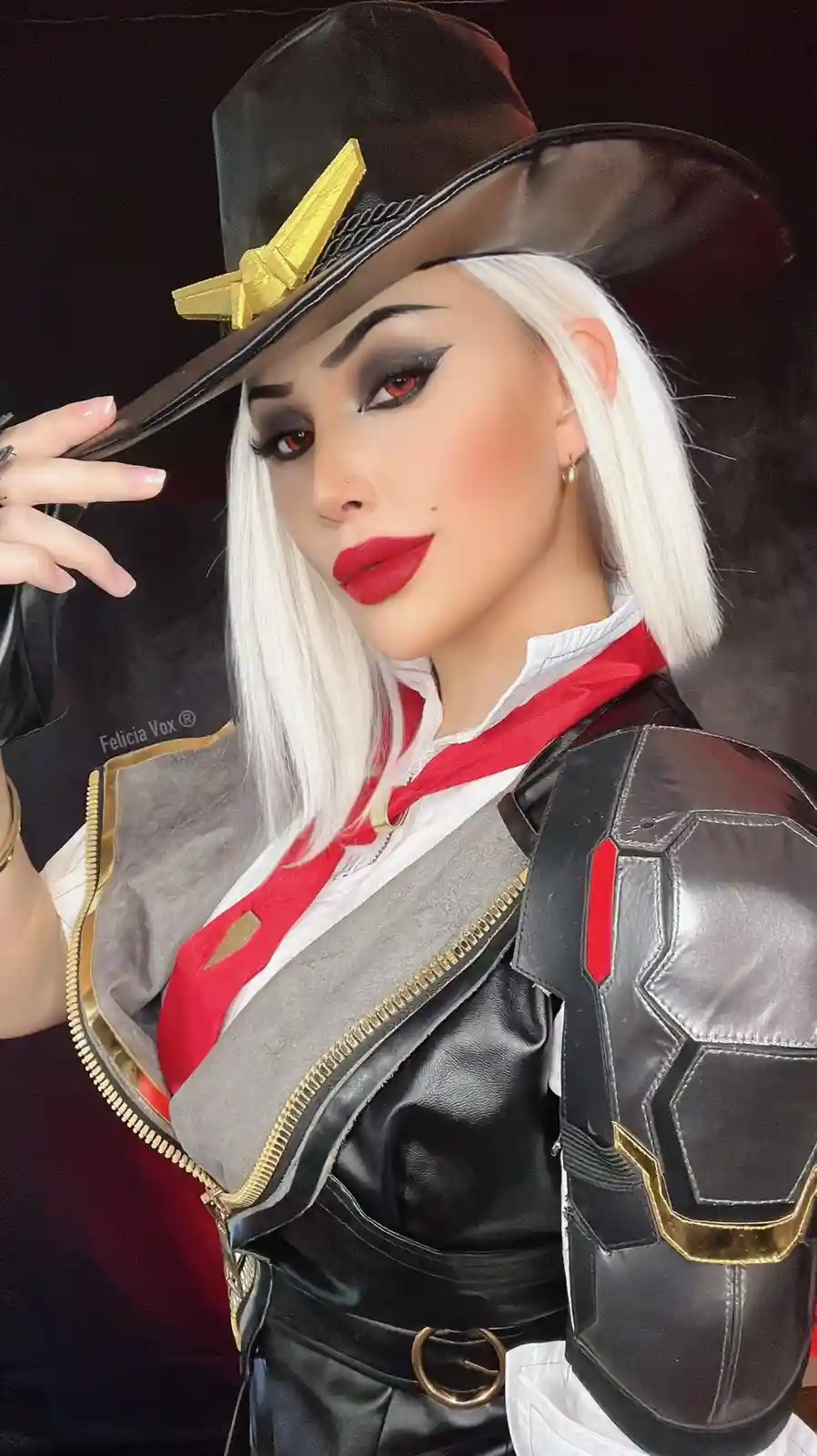 A person in a detailed cosplay of the video game character Ashe from Overwatch, wearing a black cowboy hat with a gold bow…