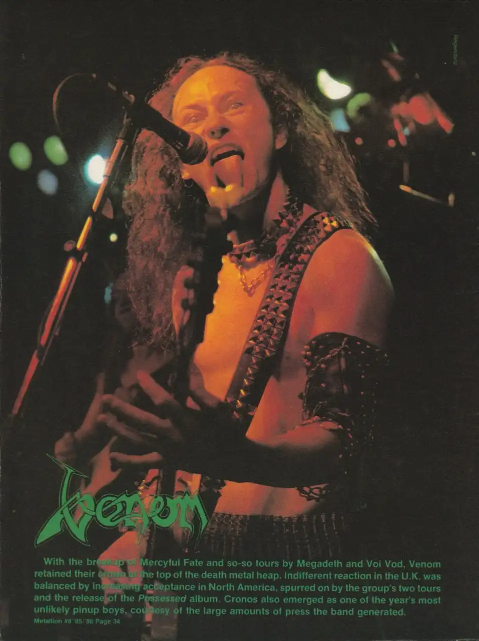 A vintage magazine photo of Venom's frontman Cronos mid-performance, tongue out, wearing spiked leather gear and holding a…