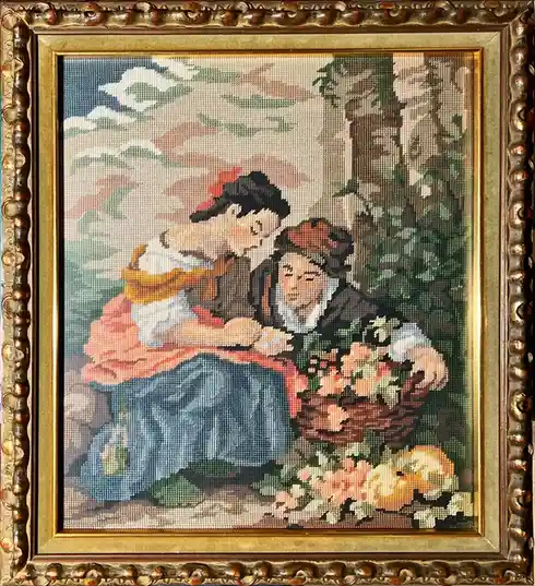 A framed needlepoint tapestry depicts two women in historical clothing, one seated and holding a basket of flowers while the…