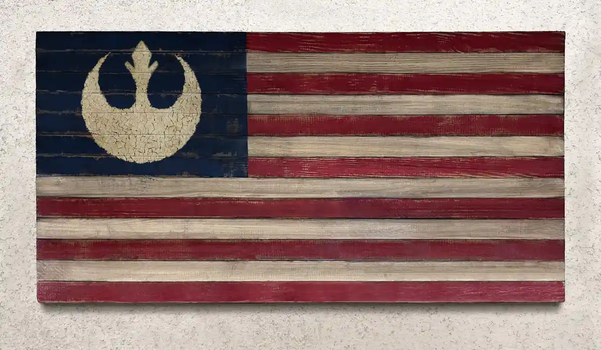 A weathered wooden flag painted to resemble the American flag, but with the canton featuring the Rebel Alliance symbol from…