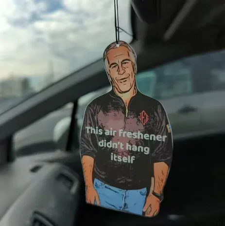 A car air freshener shaped like a smiling man in a dark zip-up jacket and blue jeans hangs from a rearview mirror. The text…