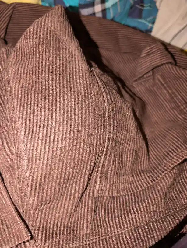 A close-up photo of a brown ribbed fabric, likely a sweater or shirt, folded and wrinkled, with a blue plaid pattern visible…