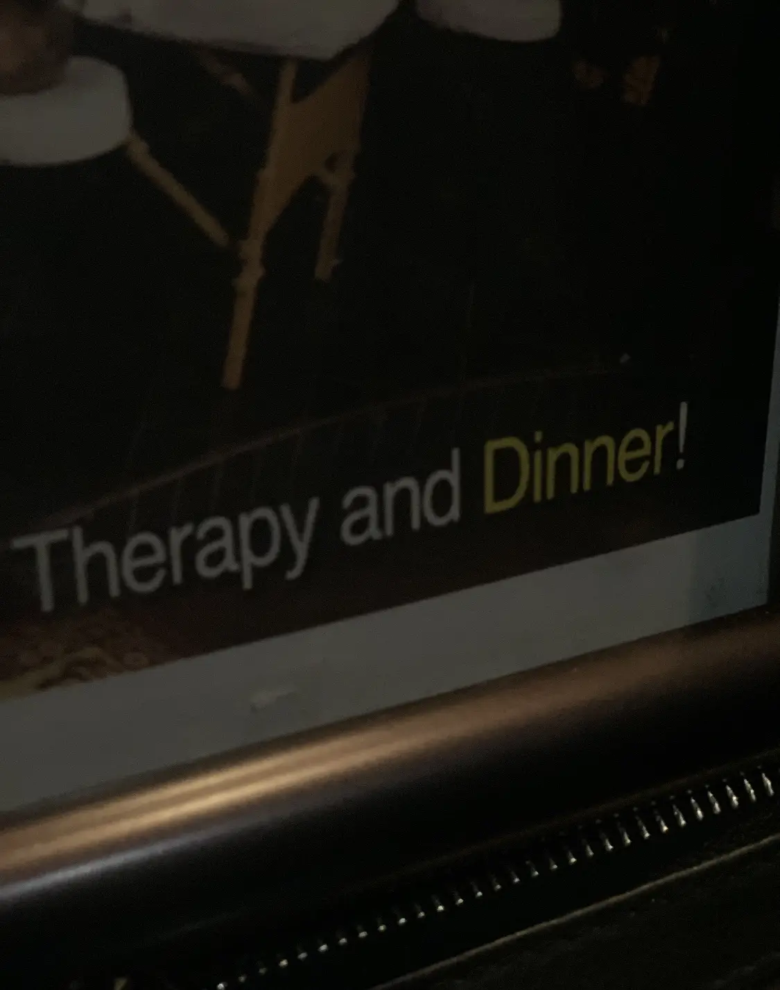 A close-up, dimly lit photo shows a framed sign with the text 'Therapy and Dinner!' in white and yellow font. The background…