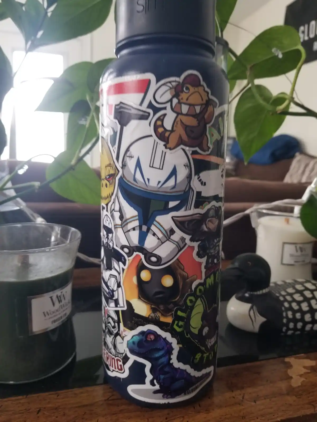 A dark blue water bottle covered in numerous colorful, overlapping stickers featuring various cartoon and video game…