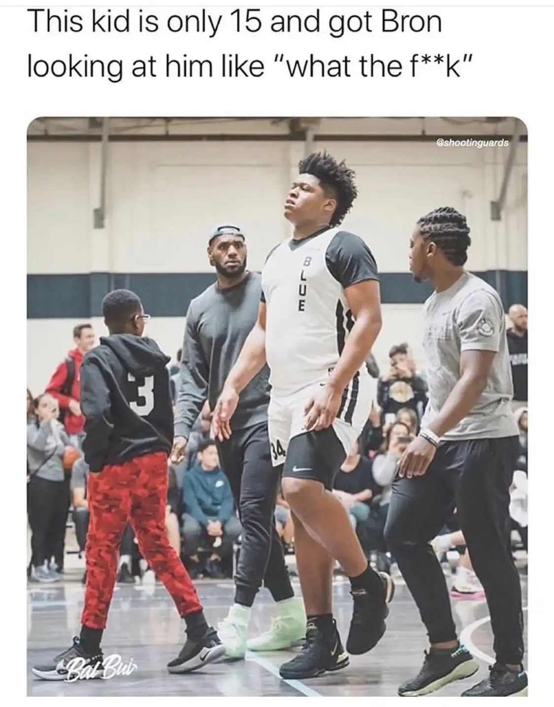 A photo shows a young boy in a black hoodie and red pants standing on a basketball court, facing away from the camera…