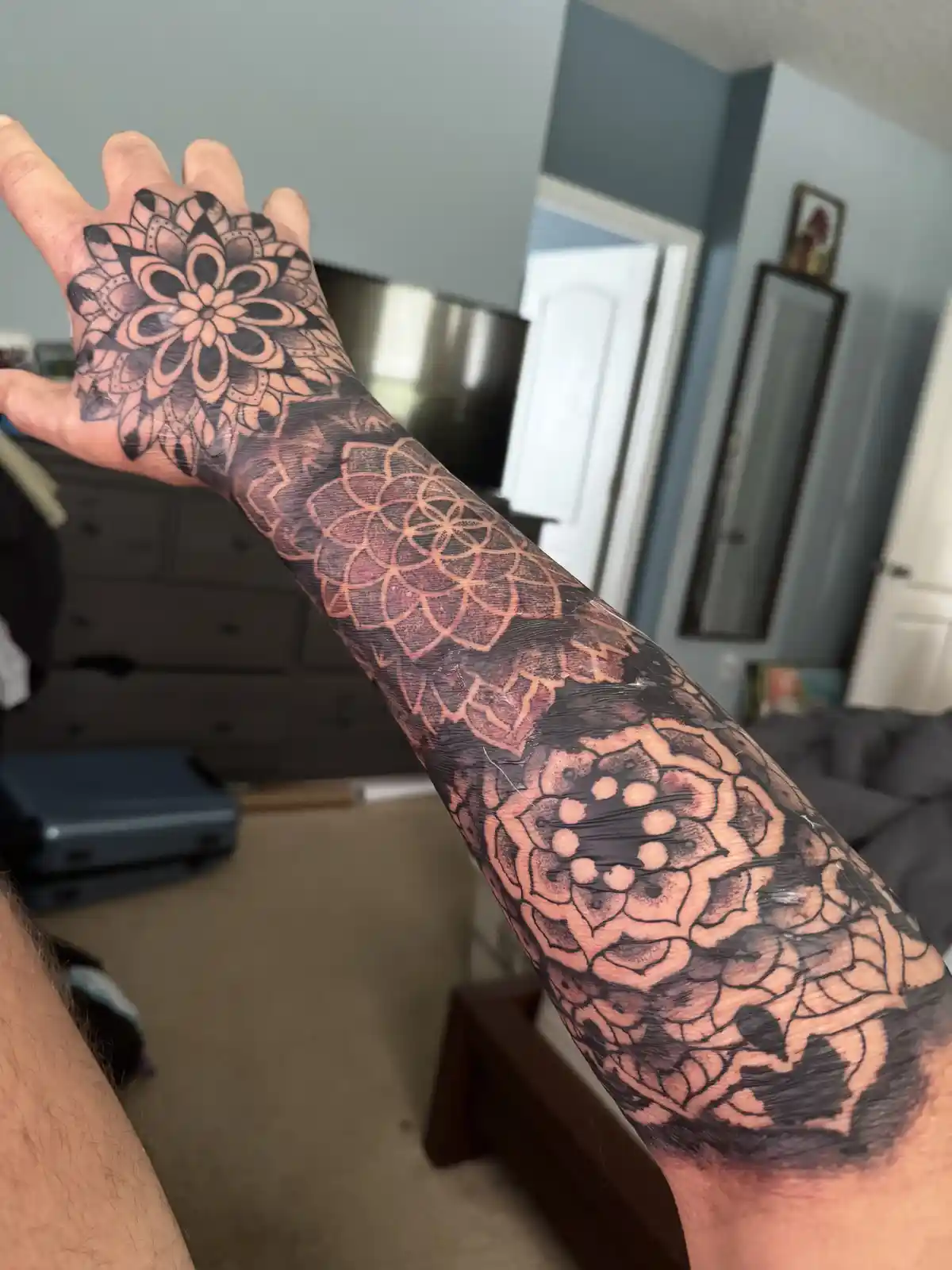A person's left arm and hand are shown with a large, intricate tattoo covering the entire forearm and hand, featuring…