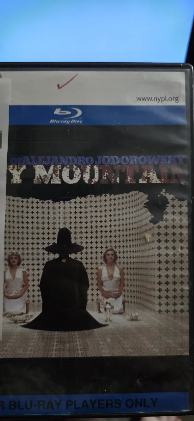 A Blu-ray disc case for Alejandro Jodorowsky's film 'Y Mountain' shows a man in a black robe and wide-brimmed hat seated…