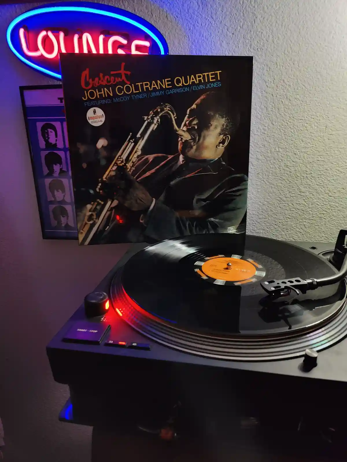 A vinyl record player with a John Coltrane 'Crescent' album cover standing upright behind it, a record spinning on the…