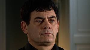 a close-up of a man with dark hair and a black shirt, his face contorted in a look of extreme disbelief or shock, with wide…