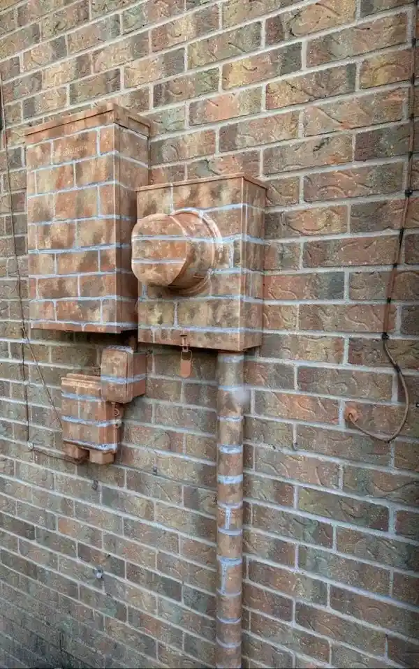 a brick wall features electrical boxes, conduits, and pipes that have been meticulously covered with matching bricks and…