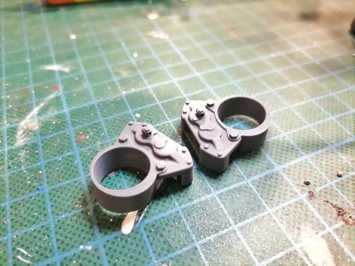 Two gray 3D-printed model kit parts, shaped like handcuffs, sit on a green grid cutting mat. The overlaid text reads 'i made…