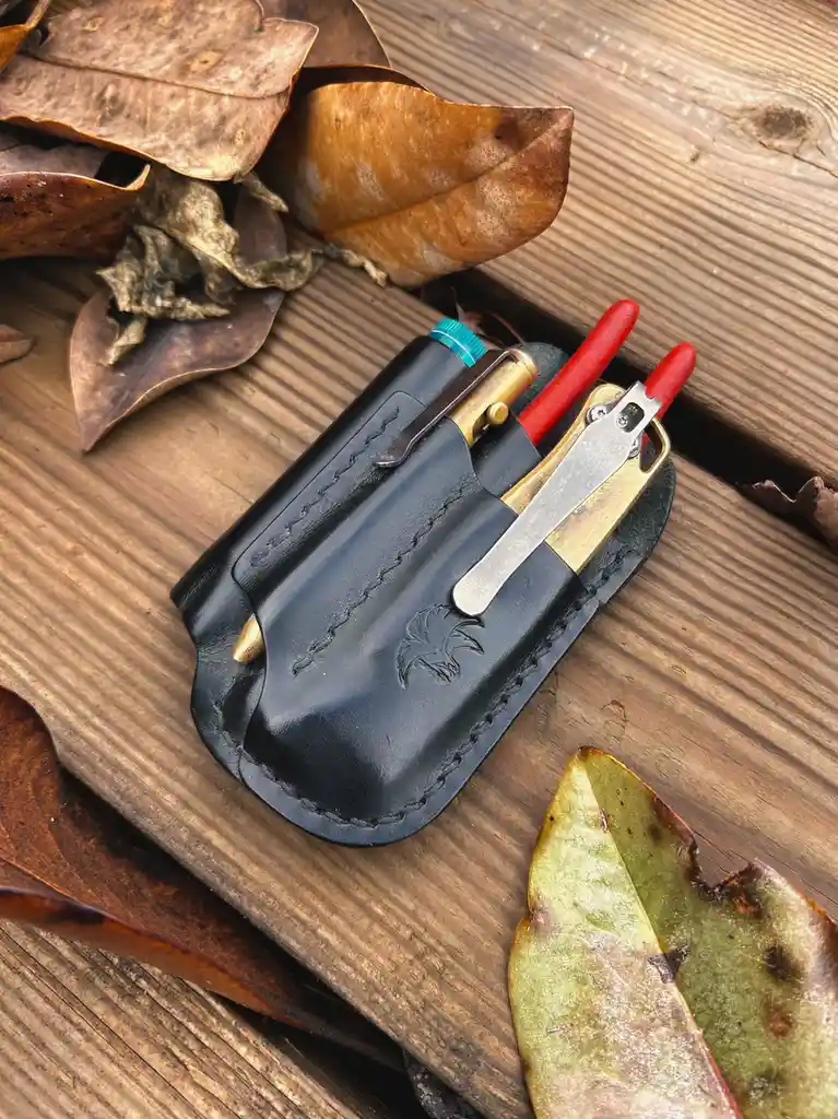 A black leather holster with visible stitching and an embossed bird design holds a brass and silver lighter with a turquoise…