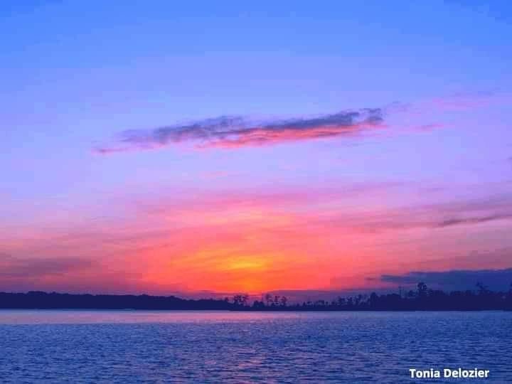 A serene sunset over a calm body of water, with vibrant orange and pink hues blending into a purple-blue sky above a distant…